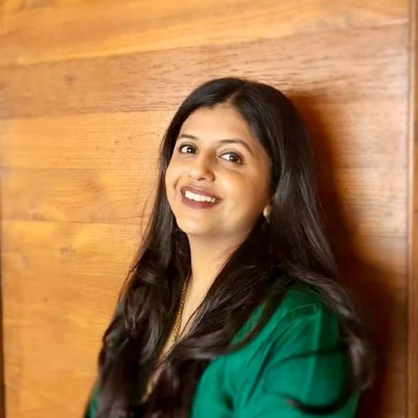 Upasana Makati in a green kurta, smiling, against a wooden wall